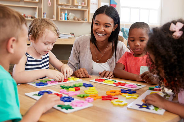 Children playing puzzles together at a table with a child care employee
